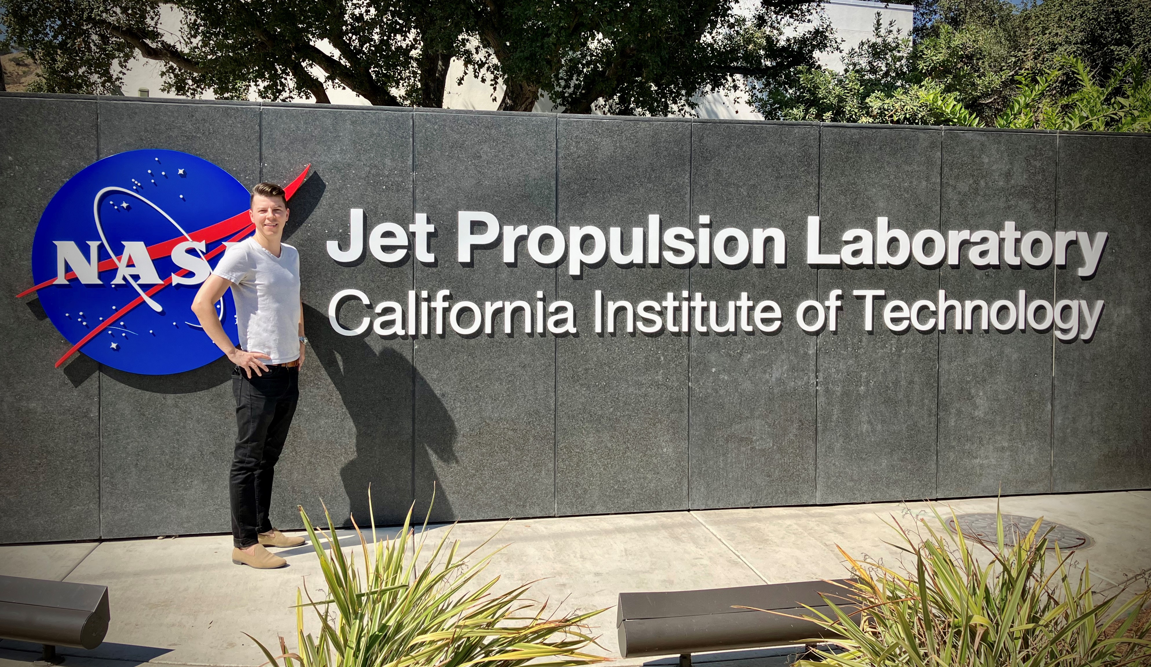 Matthäus Kiel stands in front of the big sign outside the JPL gates that says "Jet Propulsion Laboratory" next to the NASA logo