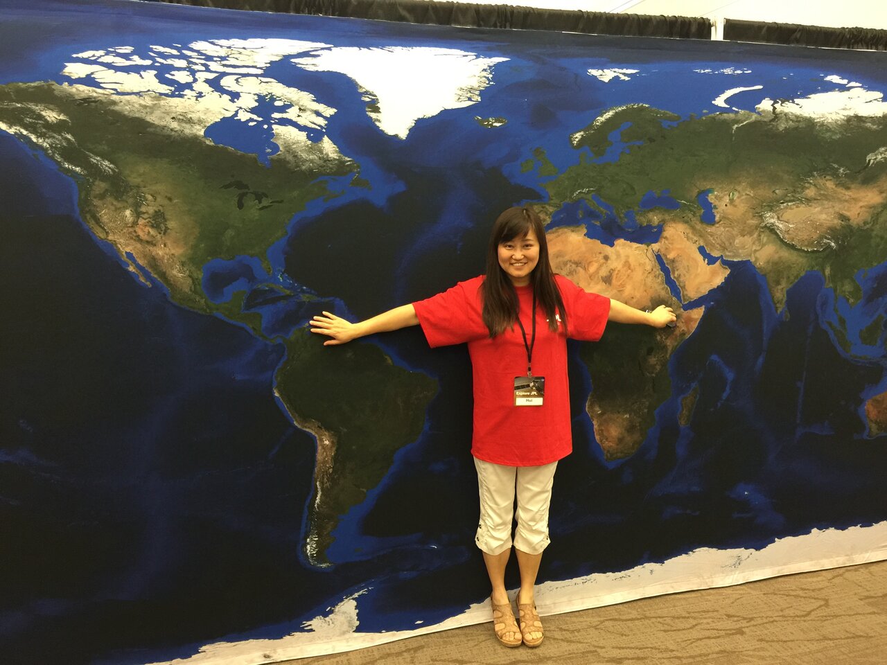 Hui Su standing in front of a map of the globe at the JPL Open House.