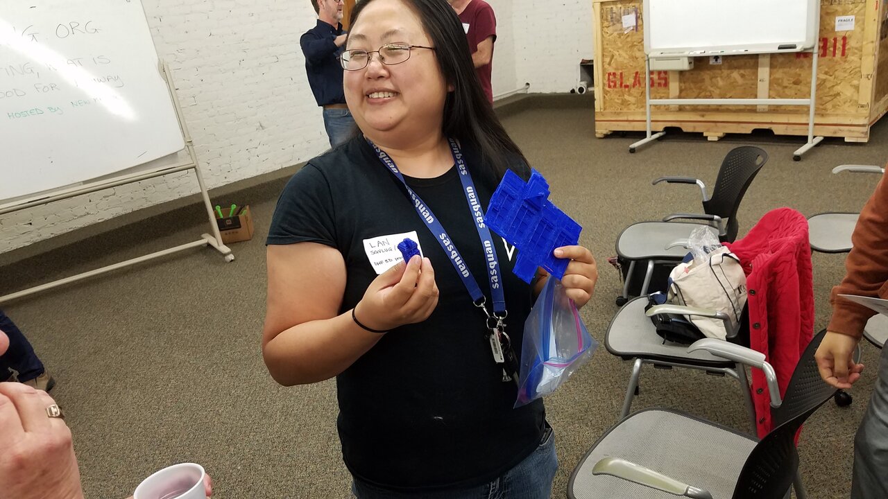 Lan Dang stands in a room, with others in the background, holding material for the tech demonstration/exploration they are working on. 